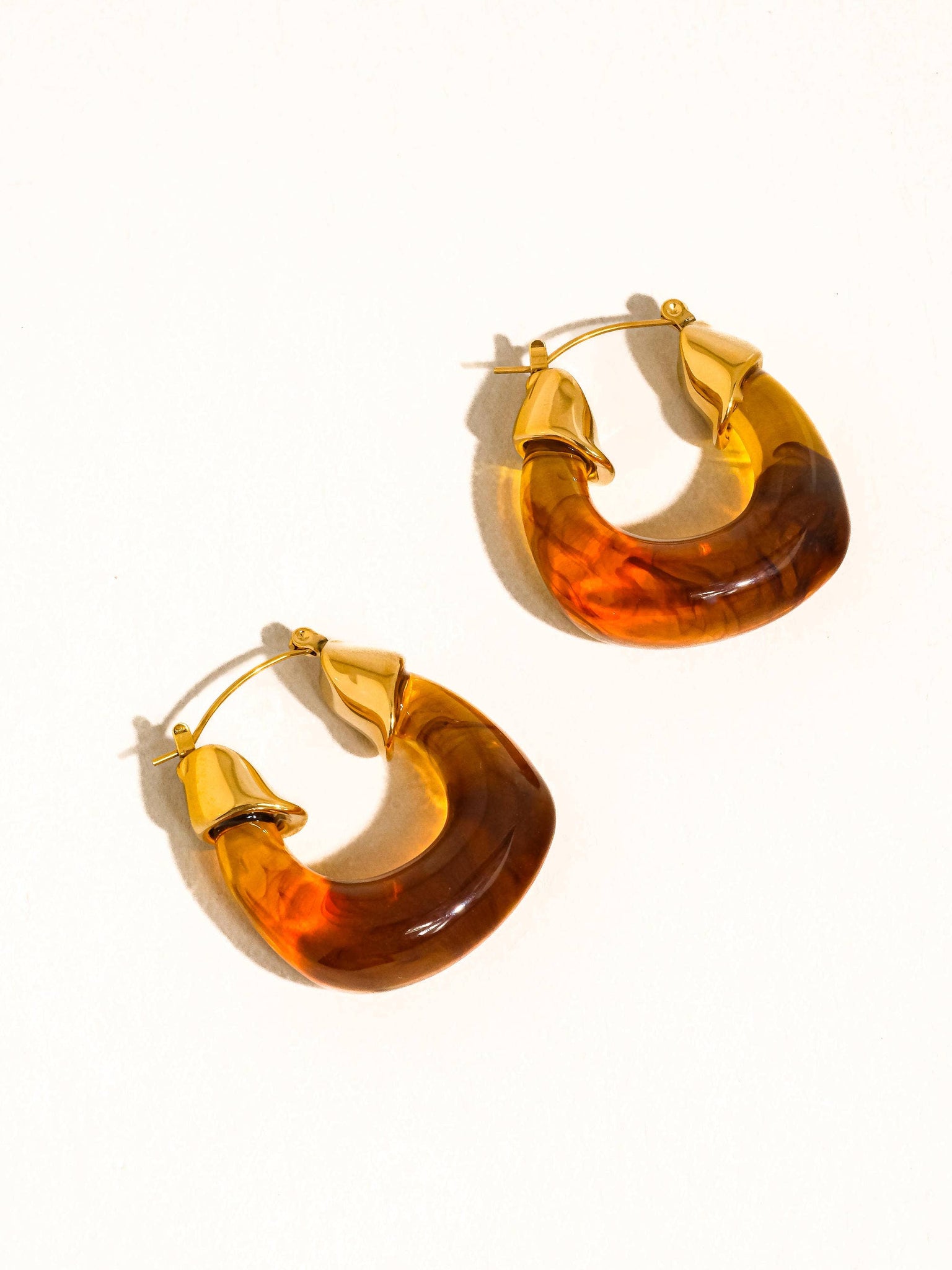 Pair of gold hoop earrings with amber-colored stones on a white background