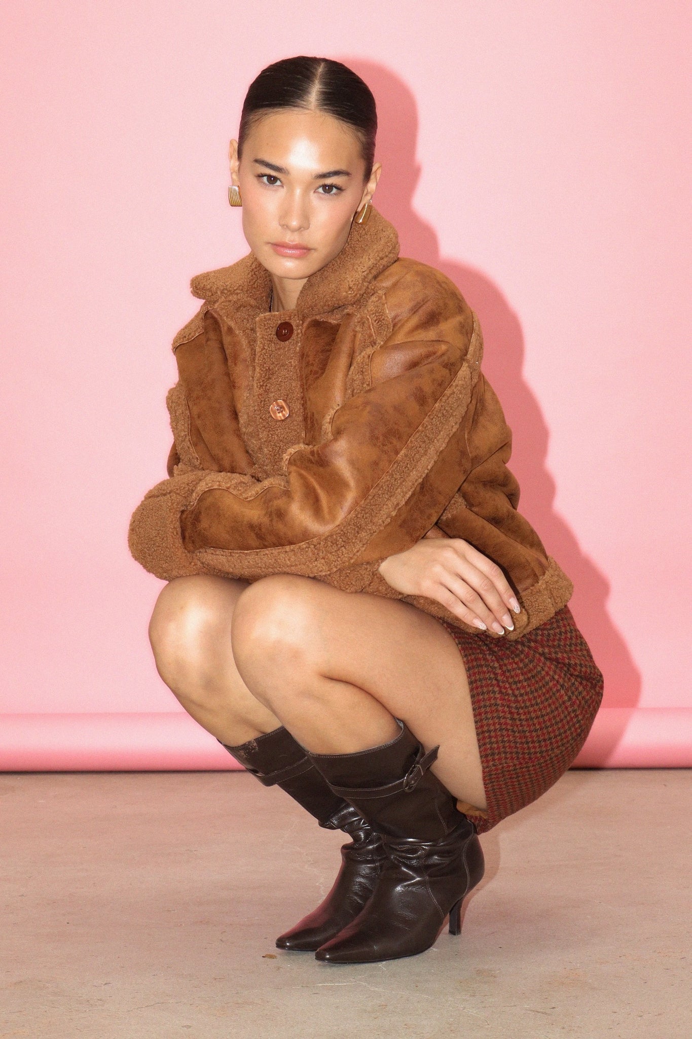 Woman wearing a brown fur coat and boots against a pink background
