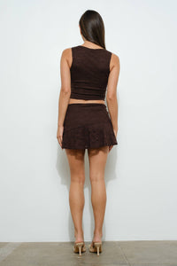 Woman wearing a brown sleeveless top and skirt set against a white background