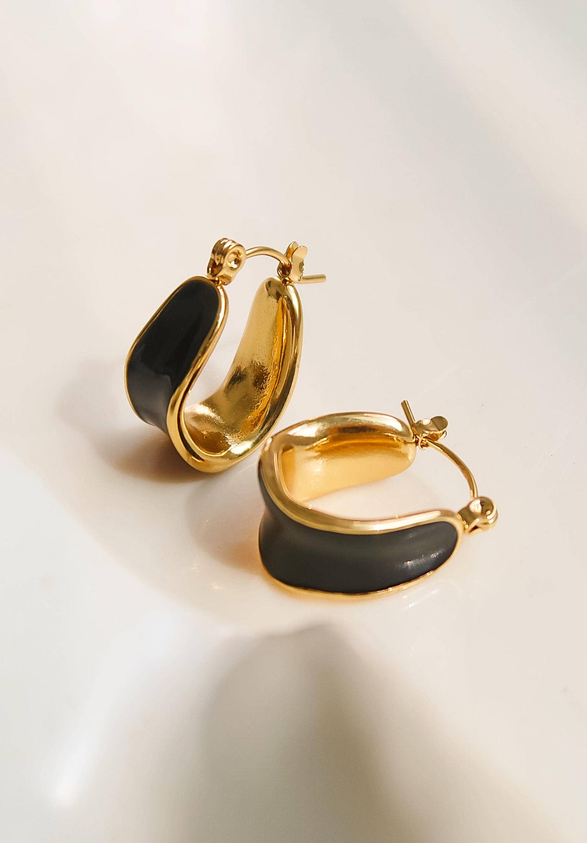Gold hoop earrings with black stones on a light background
