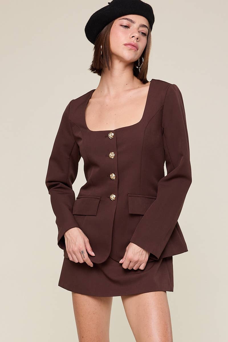 Woman wearing a brown blazer dress with gold buttons on a beige background