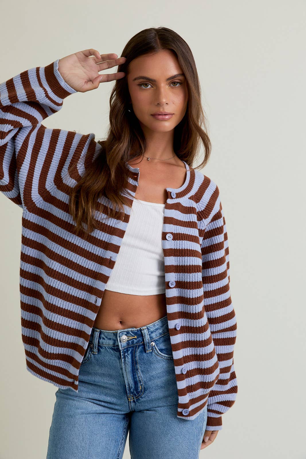 Woman wearing a brown and white striped cardigan over a white top and blue jeans, posing against a plain background.
