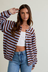 Woman wearing a brown and white striped cardigan over a white top and blue jeans, posing against a plain background.