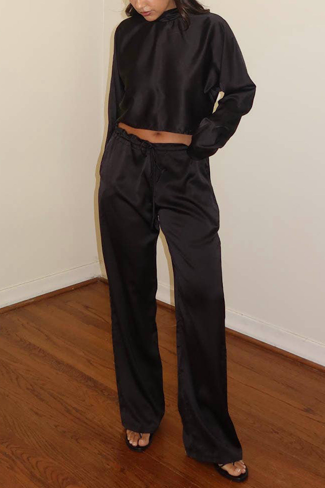 Person wearing a black outfit standing on a wooden floor with a white wall background