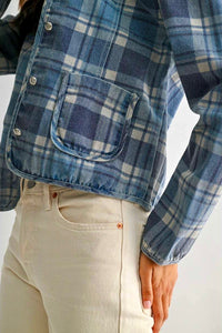 Person wearing a blue plaid shirt with a pocket on a white background