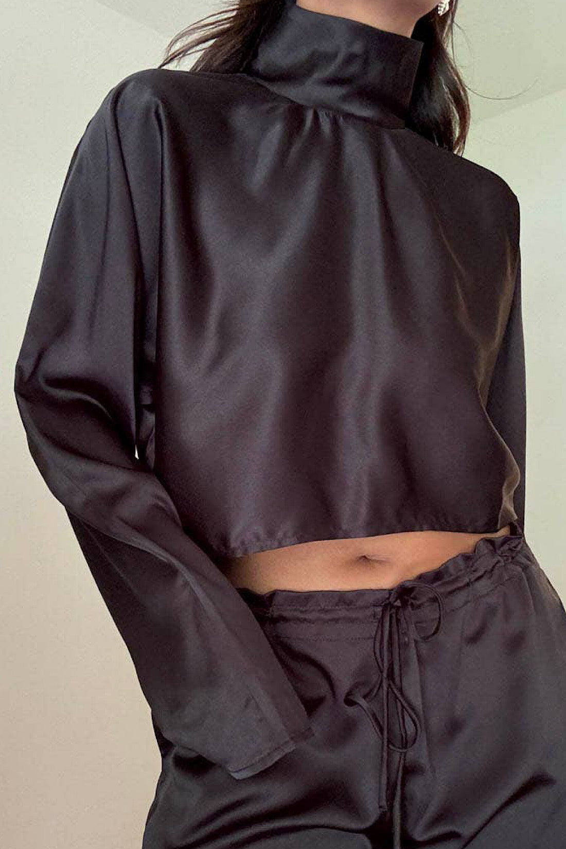 Person wearing a black satin outfit with a high neckline against a neutral background