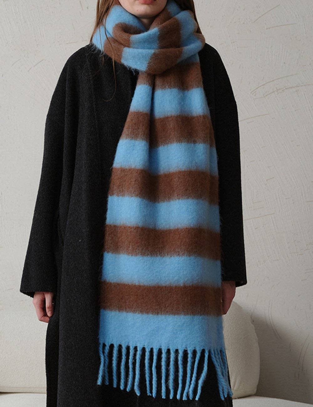 Person wearing a large blue and brown striped scarf with a plain background